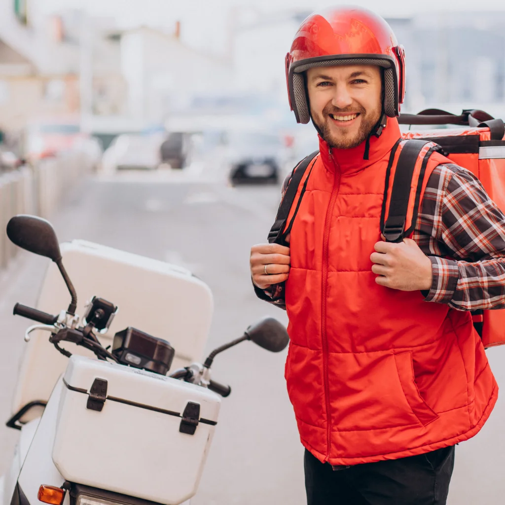 Trabajador independiente colombiano, conductor de plataforma de unos 32 años, revisando su celular con una notificación de "Examen aprobado - Certificado listo". Viste chaqueta reflectiva azul, gorra y lleva un casco de moto apoyado en su cadera. Está de pie en una calle urbana de Bogotá o Medellín, con edificios y tráfico de fondo. Su expresión es de alivio y satisfacción, como si hubiera resuelto un problema urgente. Sobre la imagen, texto superpuesto en tipografía moderna: "Guía para independientes - Tu examen ARL, sin EPS, sin filas". Fondo con acentos en Naranja Energía (#E8762B), color de MEI Movimiento. Servicio de salud laboral digital para trabajadores independientes, conductores, domiciliarios, albañiles y emprendedores - Mi Examen de Ingreso