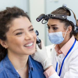 Profesional de la salud ocupacional realizando prueba de audiometría a trabajador industrial con protectores auditivos en cabina insonorizada. Evaluación de decibeles y frecuencia auditiva según normativa ARL colombiana.