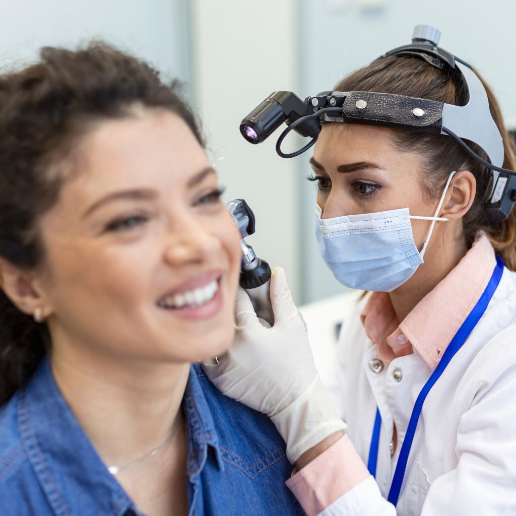 Profesional de la salud ocupacional realizando prueba de audiometría a trabajador industrial con protectores auditivos en cabina insonorizada. Evaluación de decibeles y frecuencia auditiva según normativa ARL colombiana.