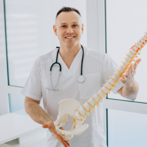 Médico especialista evaluando la movilidad de columna de un trabajador de construcción que finaliza su contrato. El paciente realiza una prueba de flexión lumbar mientras el médico observa y toma notas en una tablet. Al fondo, una obra en construcción. Documento de certificado de retiro con sello de "Válido ante ARL" sobre una mesa.