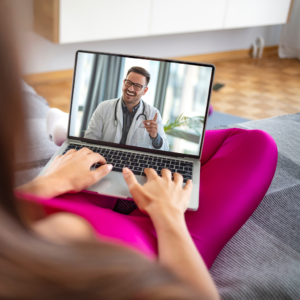 Médico especialista en Medicina Laboral realizando una videollamada con un paciente desde su computadora portátil. En la pantalla se ve al trabajador desde su hogar. Ambiente de telemedicina, moderno y accesible. Elementos visuales de tecnología médica.